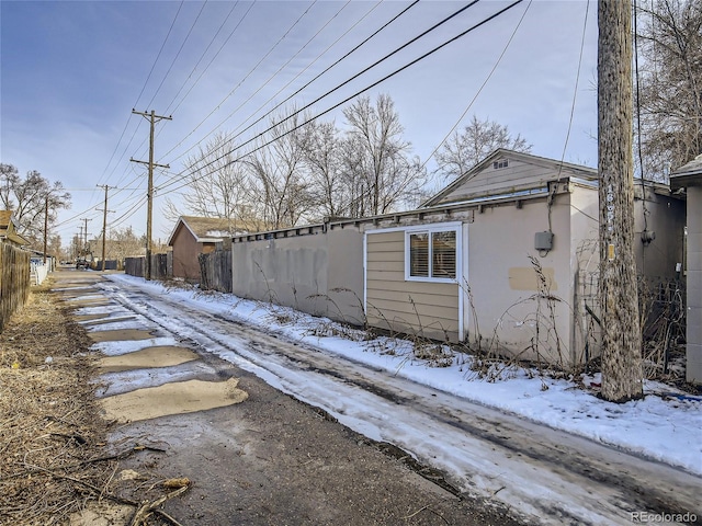snow covered property featuring fence and stucco siding