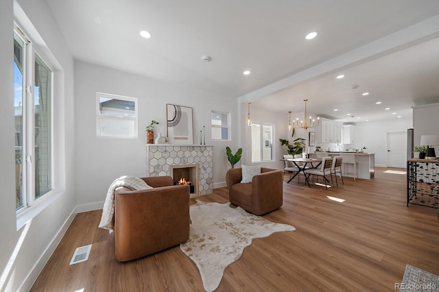 living room with a notable chandelier, a fireplace, and light wood-type flooring