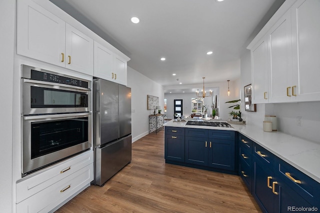 kitchen with blue cabinetry, white cabinetry, appliances with stainless steel finishes, kitchen peninsula, and pendant lighting