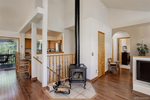 living area featuring high vaulted ceiling, wood finished floors, arched walkways, baseboards, and a wood stove