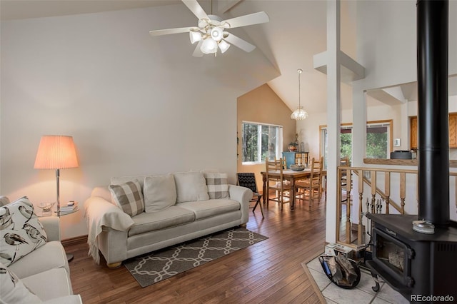 living room featuring high vaulted ceiling, ceiling fan, a wood stove, and hardwood / wood-style flooring