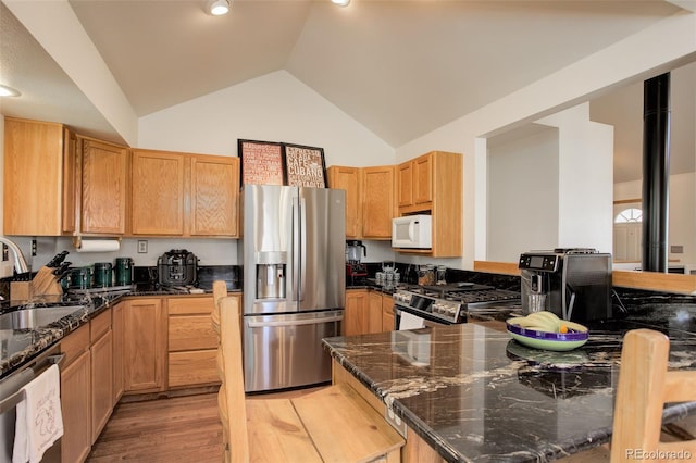 kitchen featuring dark stone counters, light wood-style flooring, appliances with stainless steel finishes, and a sink