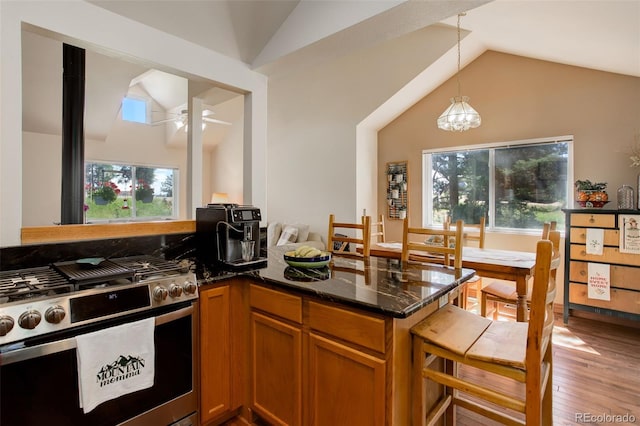 kitchen featuring gas range, dark stone counters, brown cabinets, and vaulted ceiling