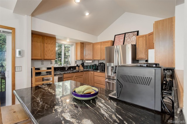 kitchen with vaulted ceiling, dark stone countertops, stainless steel refrigerator with ice dispenser, brown cabinetry, and a sink