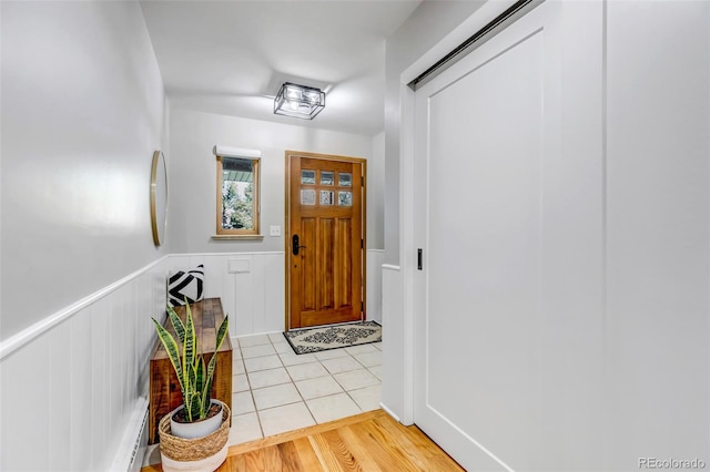 doorway with light wood finished floors and a wainscoted wall