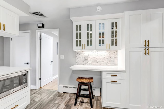 kitchen with decorative backsplash, white cabinets, stainless steel microwave, and light wood-type flooring