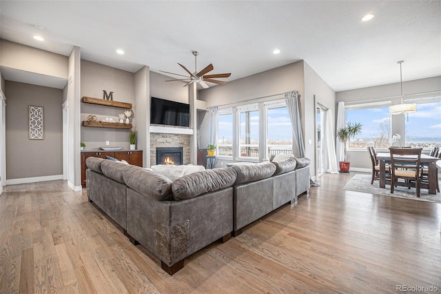 living room featuring light wood-style floors, a fireplace, baseboards, and a ceiling fan