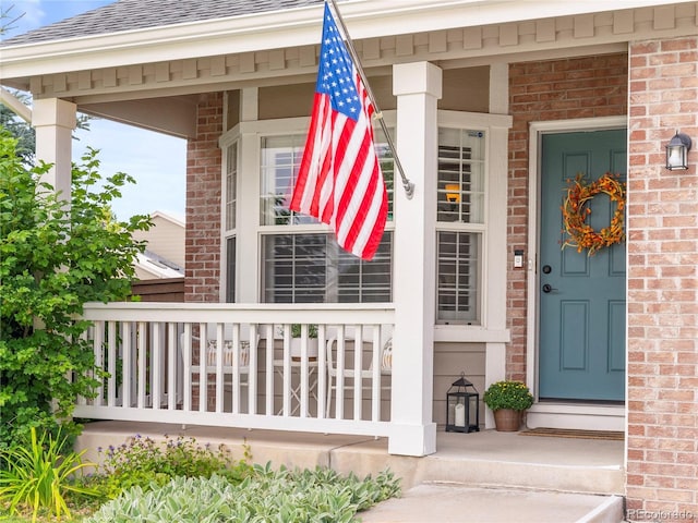 doorway to property with covered porch, a shingled roof, and brick siding