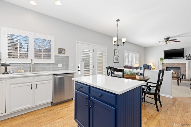 kitchen with light wood finished floors, tasteful backsplash, stainless steel dishwasher, a sink, and blue cabinets