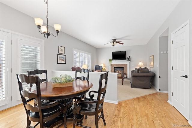 dining space featuring ceiling fan with notable chandelier, light wood-type flooring, a fireplace, and baseboards