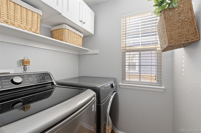 clothes washing area with a textured wall, washer and clothes dryer, and cabinet space