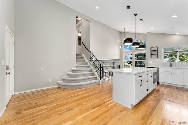 kitchen featuring light hardwood / wood-style flooring, white cabinetry, backsplash, high vaulted ceiling, and decorative light fixtures