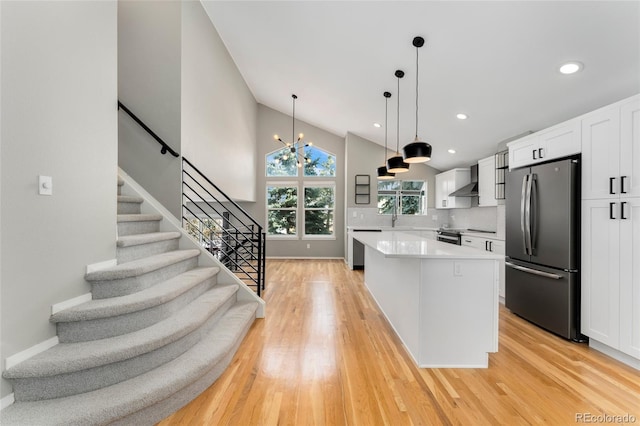 kitchen with white cabinetry, a kitchen island, stainless steel appliances, decorative backsplash, and wall chimney range hood