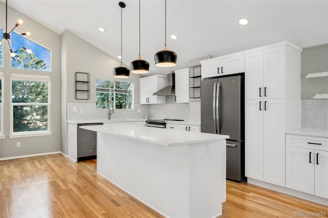 kitchen with stainless steel appliances, white cabinetry, a kitchen island, and wall chimney range hood