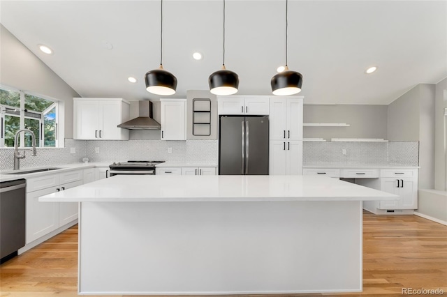 kitchen featuring sink, hanging light fixtures, appliances with stainless steel finishes, wall chimney range hood, and white cabinets