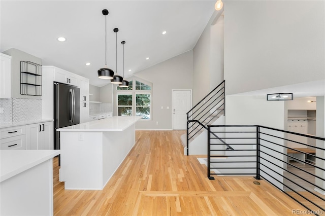 kitchen featuring pendant lighting, stainless steel refrigerator, white cabinetry, backsplash, and a center island