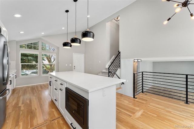 kitchen featuring vaulted ceiling, a kitchen island, pendant lighting, built in microwave, and white cabinets