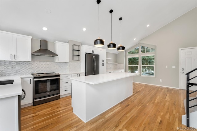 kitchen with vaulted ceiling, a kitchen island, appliances with stainless steel finishes, white cabinets, and wall chimney range hood