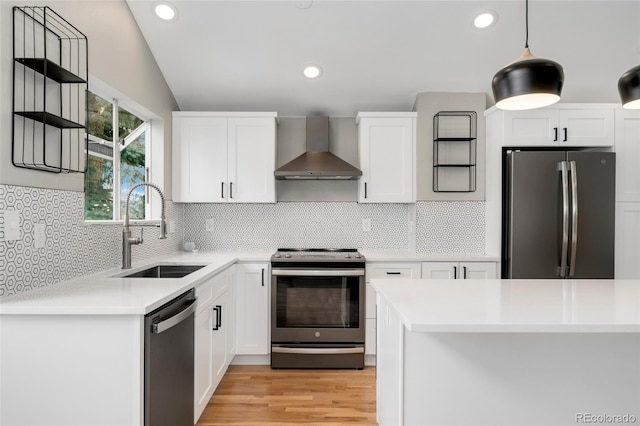 kitchen featuring wall chimney exhaust hood, sink, white cabinetry, appliances with stainless steel finishes, and pendant lighting