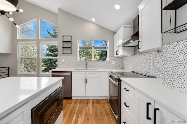 kitchen featuring sink, vaulted ceiling, white cabinets, stainless steel appliances, and wall chimney range hood