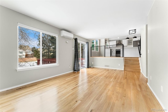 unfurnished living room with plenty of natural light, a wall mounted air conditioner, and light wood-type flooring