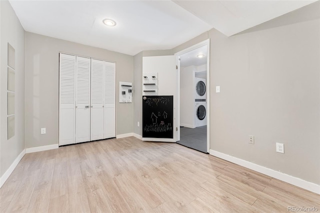 clothes washing area with light hardwood / wood-style floors and stacked washer / dryer