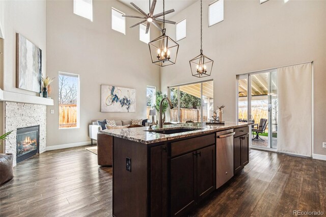 kitchen featuring a stone fireplace, dark brown cabinets, open floor plan, and a sink