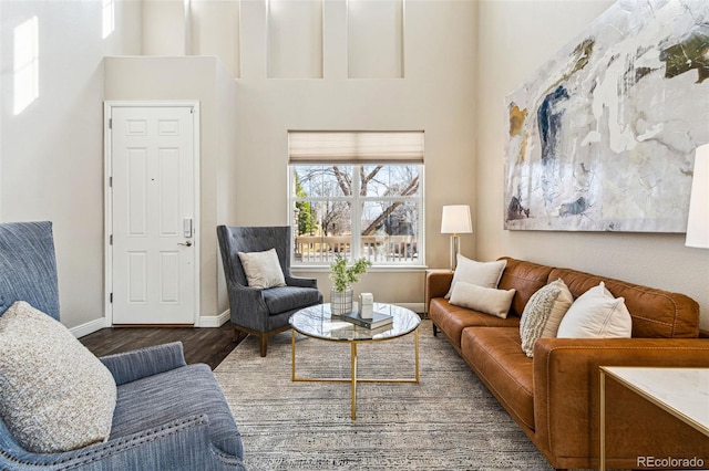 living room featuring a towering ceiling, baseboards, and wood finished floors