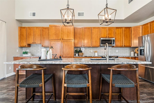 kitchen with light stone countertops, visible vents, an inviting chandelier, stainless steel appliances, and dark wood-type flooring