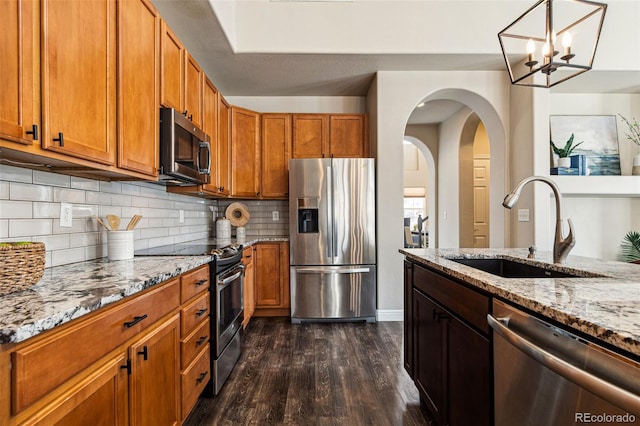 kitchen with a sink, stainless steel appliances, light stone counters, and dark wood-type flooring