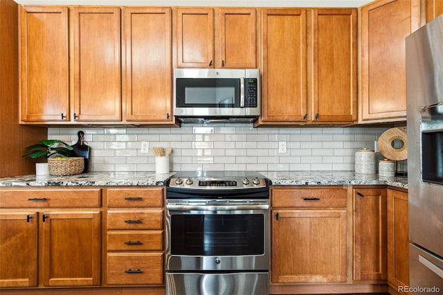 kitchen with light stone counters, backsplash, appliances with stainless steel finishes, and brown cabinetry