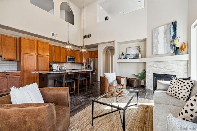 living room featuring a stone fireplace, wood finished floors, visible vents, and arched walkways