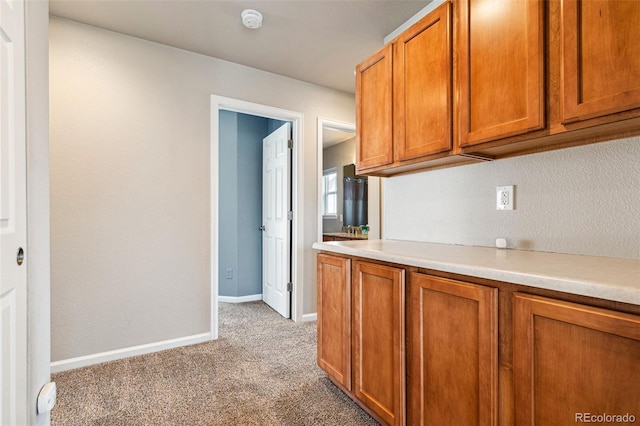 kitchen with brown cabinets, light colored carpet, light countertops, and baseboards