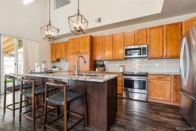 kitchen featuring dark wood finished floors, stainless steel appliances, brown cabinetry, and a sink