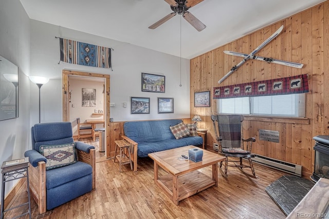 living room with ceiling fan, hardwood / wood-style floors, a baseboard heating unit, a towering ceiling, and wood walls