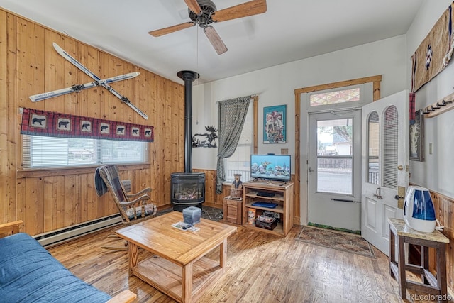 living room with ceiling fan, light hardwood / wood-style flooring, wood walls, and a wood stove