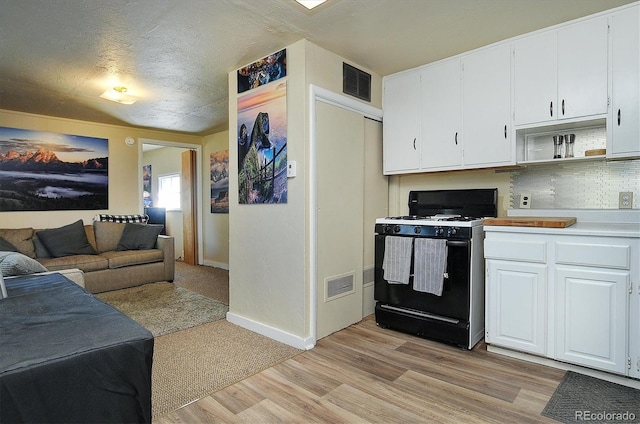 kitchen with light wood-type flooring, tasteful backsplash, white cabinetry, black gas range, and a textured ceiling