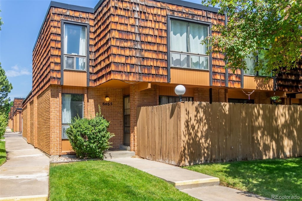 view of front facade featuring a front yard, brick siding, fence, and mansard roof