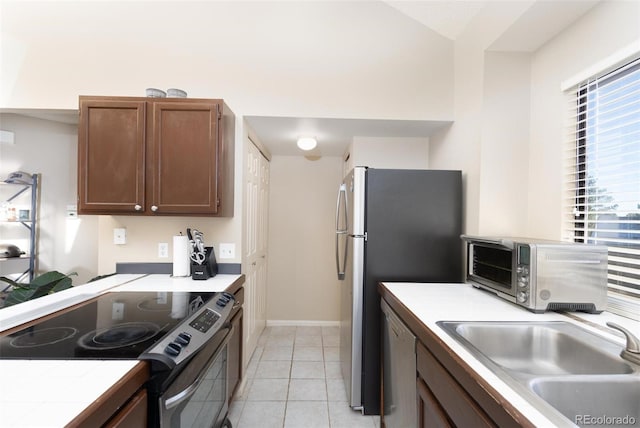 kitchen with tile countertops, sink, light tile patterned floors, and stainless steel appliances