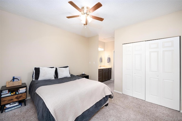 bedroom with ceiling fan, ensuite bathroom, a textured ceiling, light carpet, and a closet