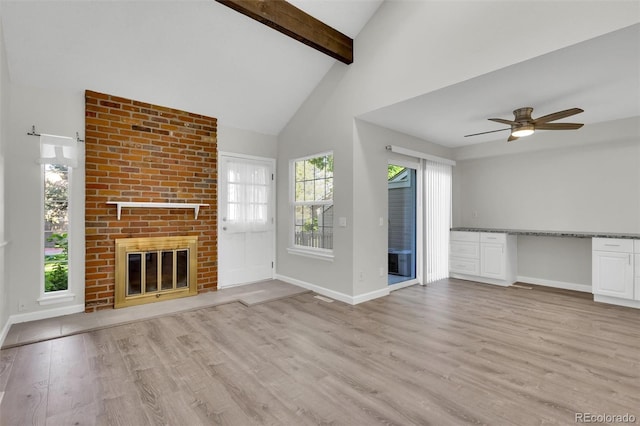 14243 E Radcliff Cir, Aurora, CO 80015 - unfurnished living room with a brick fireplace, light wood-style flooring, healthy amount of natural light, beam ceiling, and ceiling fan