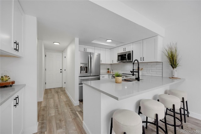 kitchen featuring backsplash, light wood-type flooring, a kitchen breakfast bar, white cabinets, and stainless steel appliances