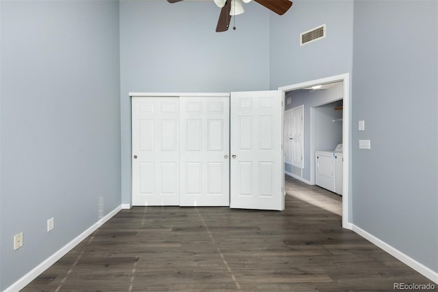 unfurnished bedroom with dark wood-type flooring, ceiling fan, independent washer and dryer, a towering ceiling, and a closet