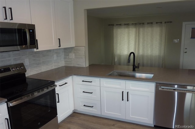 3575 W 9th Ave, Denver, CO 80204 - kitchen with appliances with stainless steel finishes, backsplash, white cabinetry, wood finished floors, and a peninsula