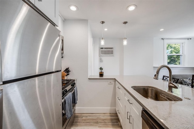 kitchen with a wall unit AC, sink, white cabinets, stainless steel fridge, and range with gas stovetop