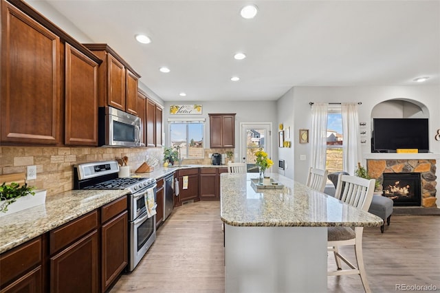 10649 Mt Emerald Dr, Peyton, CO 80831 - kitchen with appliances with stainless steel finishes, a breakfast bar, a kitchen island, a stone fireplace, and light wood-type flooring