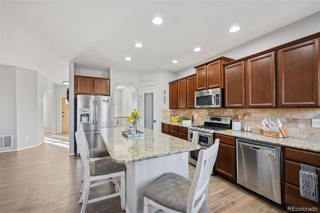 10649 Mt Emerald Dr, Peyton, CO 80831 - kitchen with stainless steel appliances, arched walkways, a kitchen breakfast bar, light wood-style floors, and decorative backsplash