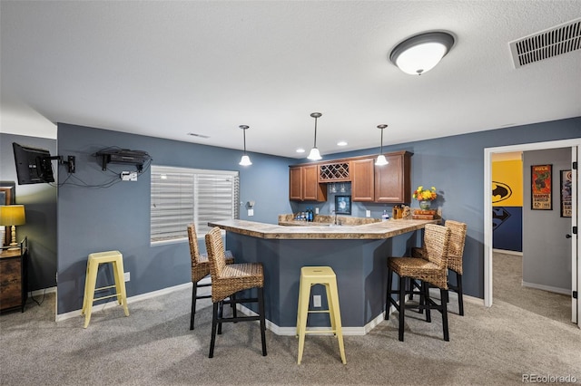 10649 Mt Emerald Dr, Peyton, CO 80831 - kitchen with a breakfast bar, a peninsula, light colored carpet, brown cabinetry, and decorative light fixtures