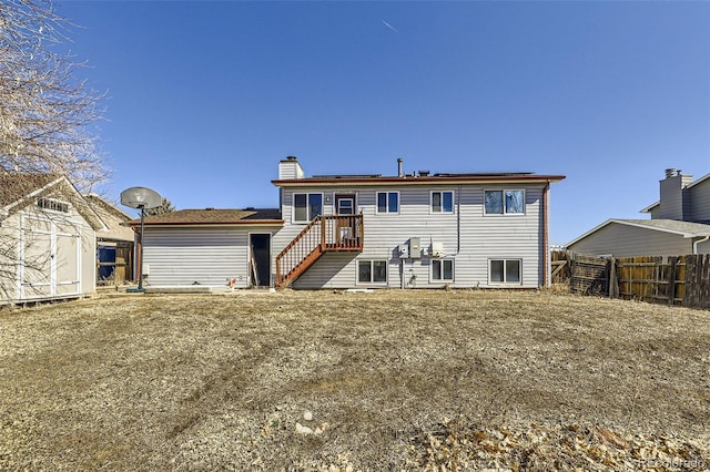 rear view of house with a storage shed, solar panels, a chimney, an outbuilding, and fence