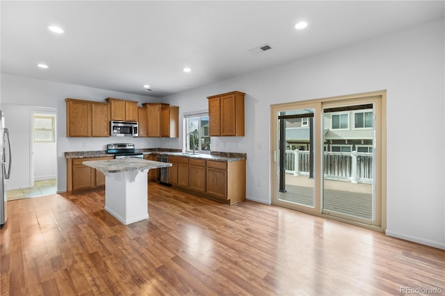 kitchen with light wood-type flooring, light stone counters, appliances with stainless steel finishes, a kitchen island, and a kitchen bar